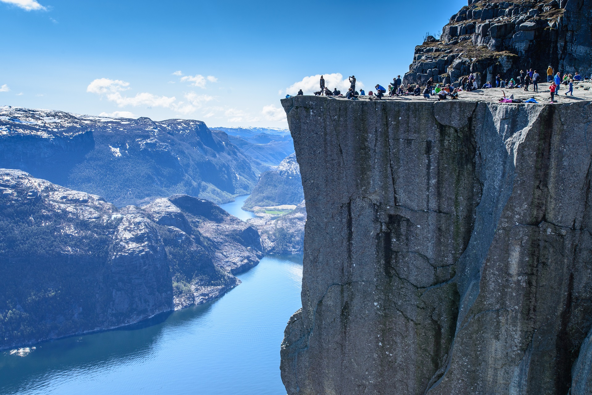 Steile Felsklippe mit vielen Touristen. Im Hintergrund ein Fjord. 