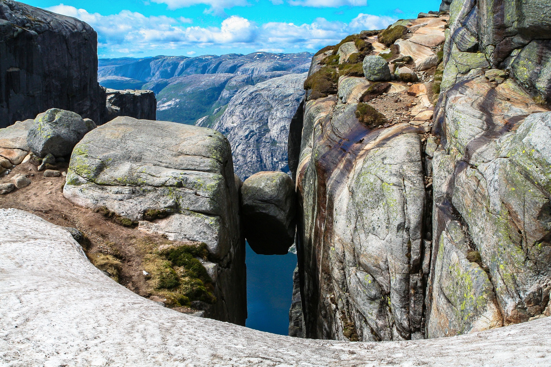 Großer runder Felsblock eingeklemmt zwischen zwei steilen Felswänden hoch über einem Fjord in einer norwegischen Berglandschaft.
