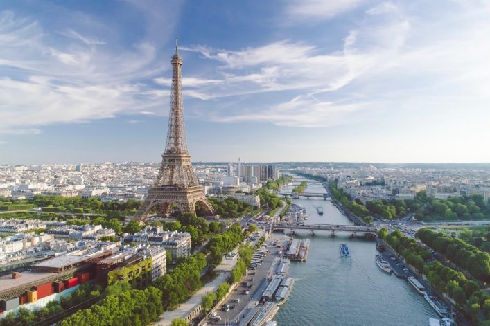 Luftaufnahme von Paris bei Sonnenuntergang mit dem Eiffelturm im Vordergrund und der Seine, die sich durch die Stadt schlängelt.