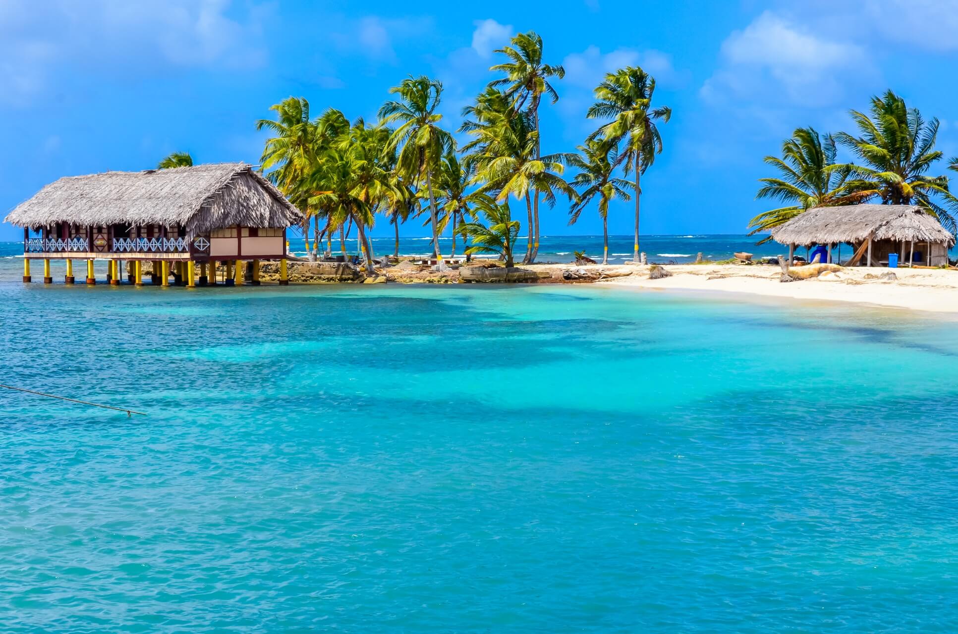 Tropische Insel mit Palmen, türkisblauem Wasser und strohgedeckten Hütten direkt am Meer.