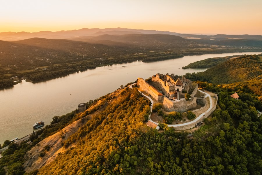 Blick aus der Vogelperspektive auf das Donauknie in Ungarn. Die grüne Landschaft erstreckt sich weit über das Land, in der Mitte fließt ein Fluss durchs Bild. Ins Auge sticht die Visegrád Citadel, die auf einem Hügel gelegene Burg.