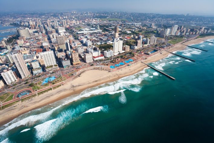 Luftaufnahme von Durban, Südafrika mit Hochhäusern, einem goldenen Strandstreifen und türkisfarbenen Wellen des Indischen Ozeans.