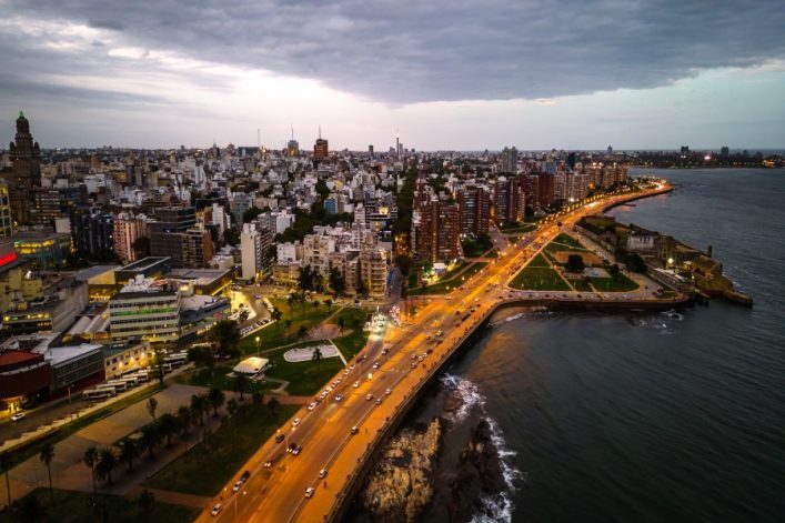 Luftaufnahme von Montevideo, Uruguay, bei Dämmerung mit beleuchteten Straßen, die sich entlang der Küste schlängeln, umgeben von dichter Bebauung.