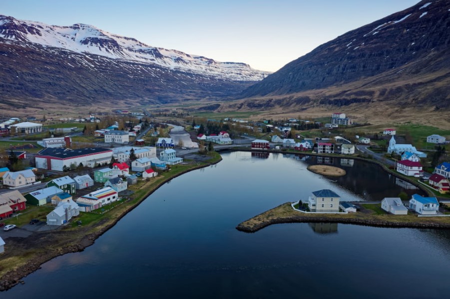 Luftaufnahme der Stadt Seydisfjoerdur in Island. Sie liegt direkt am Wasser, Ein paar Häuser stehen am Rand der hohen Bergkette im Hintergrund.