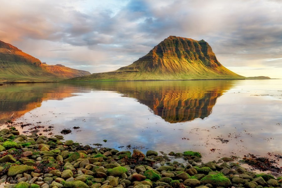 Berg in der Nähe der isländischen Stadt Grundarfjörður. Der Berg spiegelt sich in dem Wasser im Vordergrund. Der Fuß des Berges ist grün, weiter oben ist der Berg kahl.