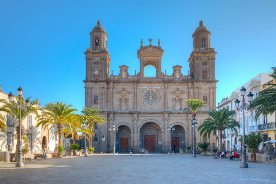 Vor der Kathedrale von Santa Ana auf Gran Canaria sitzen Familien auf Bänken unter Palmen. Der weitläufige Platz und die imposante Fassade bilden eine idyllische Kulisse für einen Familienurlaub.