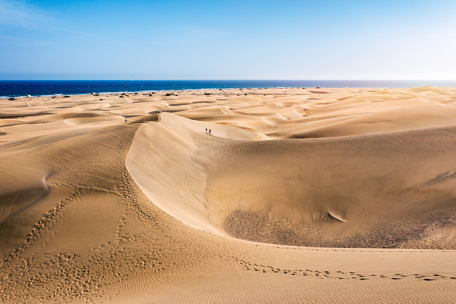 Weite Sanddünen von Maspalomas auf Gran Canaria, im Hintergrund das blaue Meer. Fußspuren durchziehen den Sand